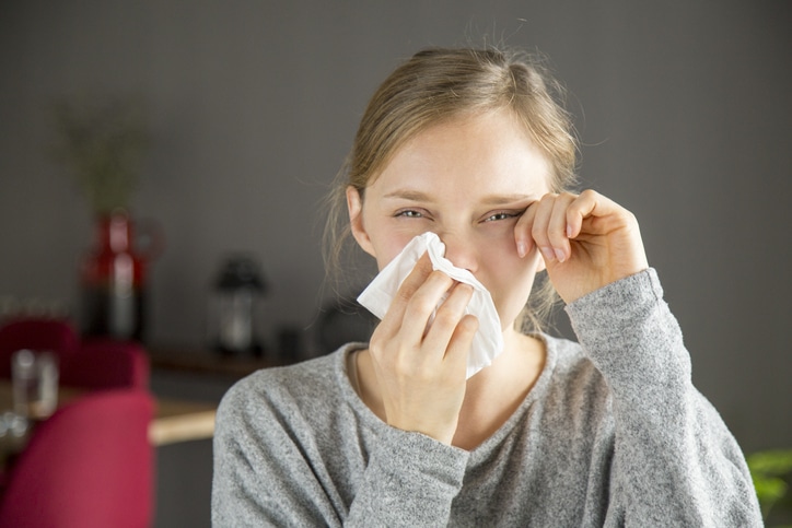 Stressed girl suffering from allergy. Young woman covering nose with tissue and moping tears from face. Allergy concept