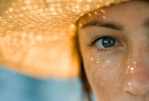 picture of top right side of woman's face wearing large sunhat with blurred background