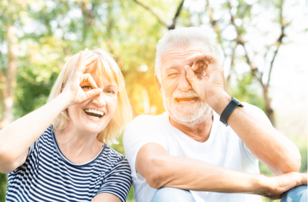 Seniors in the park with happy face smiling doing ok sign with hand on eye looking through fingers.