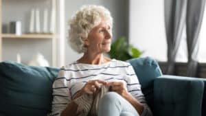 old woman sit on sofa, distracted from hand knitting