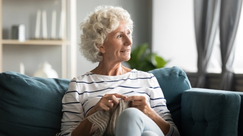 old woman sit on sofa, distracted from hand knitting