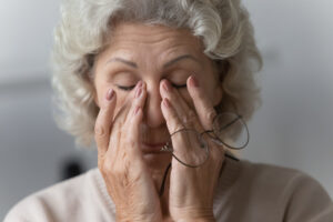 60-year-old woman takes off her glasses and rubs her eyes due to dry eye symptoms.
