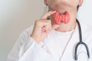 Doctor holds a model of a thyroid against her neck