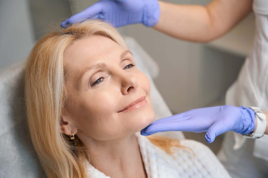 Hands in medical gloves holding happy woman head