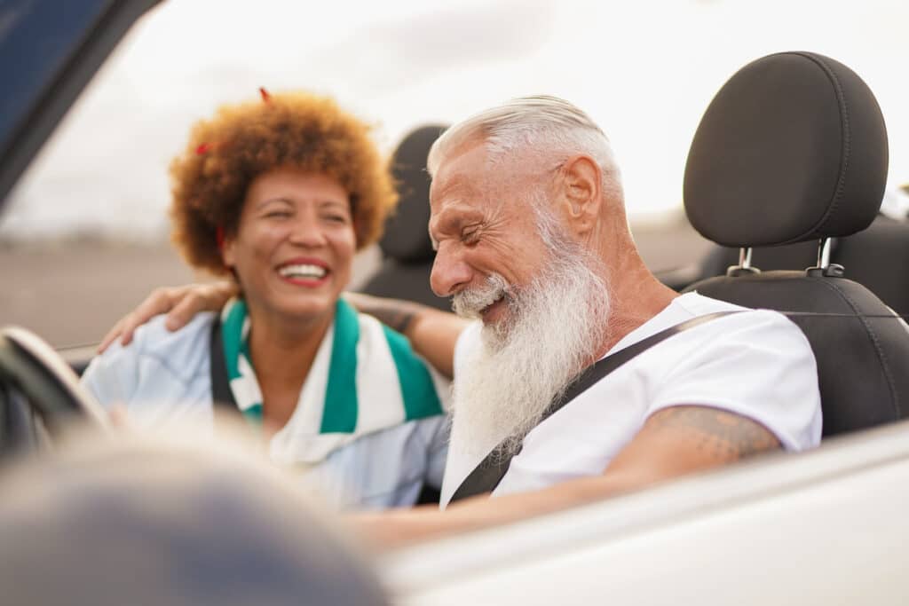 Senior couple enjoys driving around in a car with its top down.